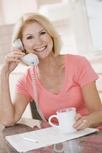 Woman in kitchen using telephone and smiling